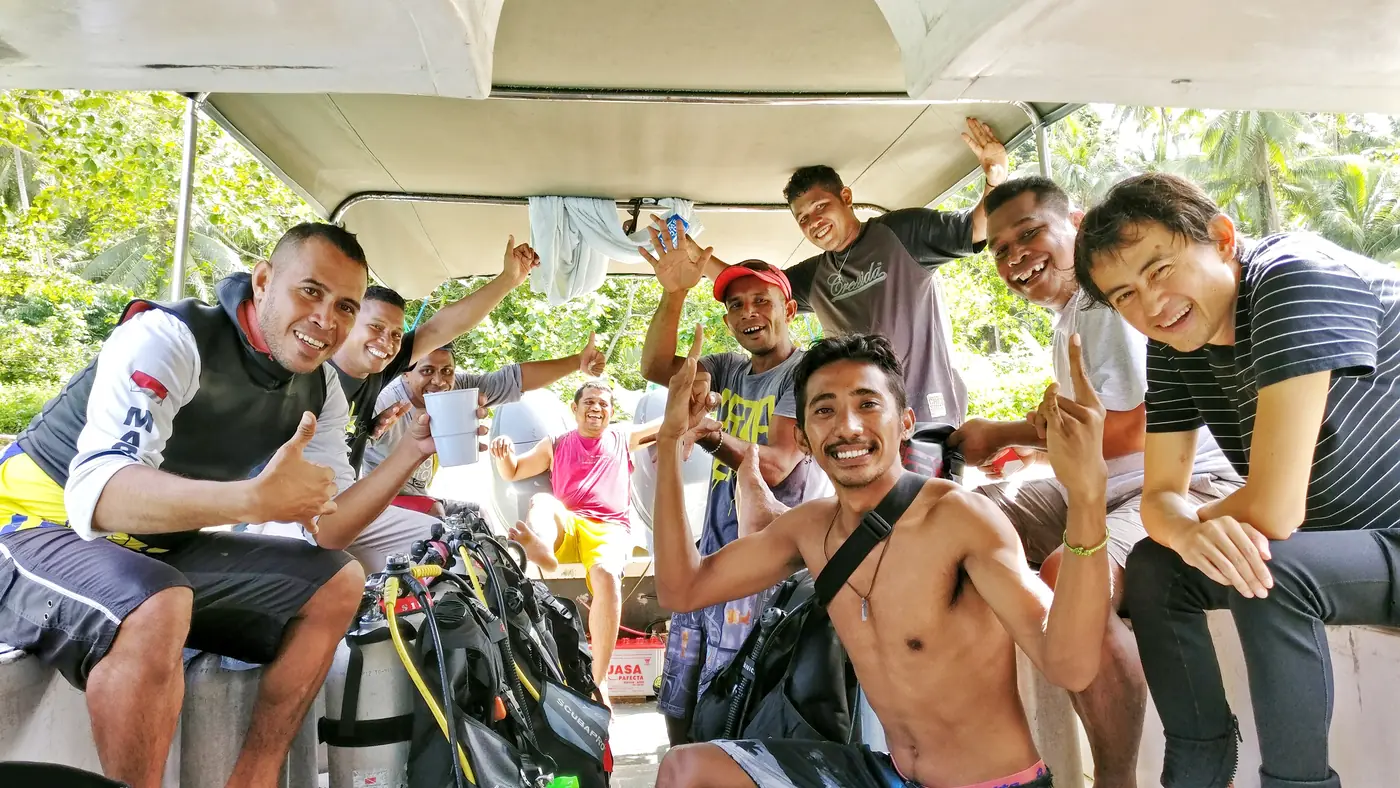 The Blue Rose Divers crew and their divers sitting under the canopy of one of the shop's speed boats, tanks and BCDs stacked between them.